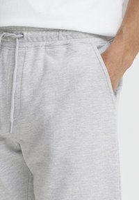 Pantalon de survêtement en coton gris avec une ceinture élastique à cordon de serrage, des poches latérales et un tissu doux et texturé.