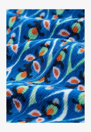 Tessuto blu con una superficie testurizzata, caratterizzato da un motivo floreale in verde, arancione e nero. Onde curve migliorano la profondità e il movimento.