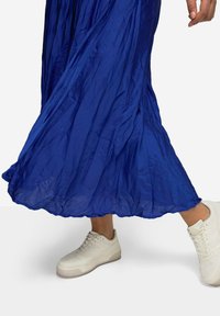 Vestido maxi de tela arrugada color azul cobalto con una silueta fluida, combinado con zapatillas blancas que presentan un diseño texturizado y lengüeta acolchada.