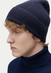 Mörkblå ribbad stickad mössa med en åtsittande passform, tillsammans med en matchande turtleneck. Slät textur och subtila sömnadsdetaljer synliga.