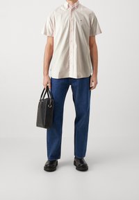 Kortärmlig lichtroze blouse met kraag en knopen, gecombineerd met een blauwe spijkerbroek. Zwarte handtas met een gestructureerd oppervlak. Zwarte schoenen.