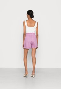 Vit ärmlös topp med fyrkantig halsringning, matchad med rosa shorts med elastisk midjeband. Modellen bär beige klackskor.