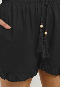 Svarta shorts med volangkant, elastisk midja och snörning med träkulor och tofsar för extra detaljer.