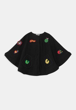 Cape noire avec poches avant, décorée de patchs colorés et ludiques incluant des fleurs, des fruits, un arc-en-ciel et le texte "SUPER".