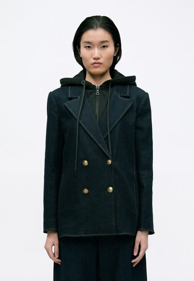 Dark denim double-breasted jacket featuring gold buttons, a structured design, and prominent lapels, layered over a black zippered hoodie.