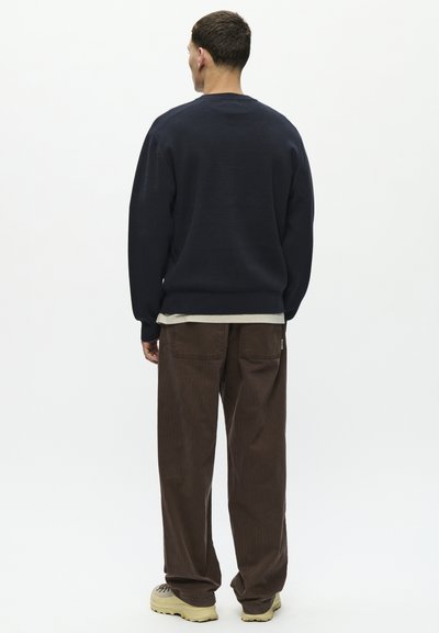Suéter azul marino con un corte relajado y cuello redondo, combinado con pantalones de pana marrones. La prenda presenta una textura de tela y un estilo casual.