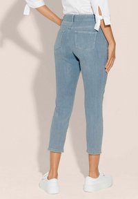 Hellblaue Denim-Caprihosen mit einer taillierten Passform, mittelhohem Bund und zwei Gesäßtaschen, kombiniert mit weißen Sneakern.