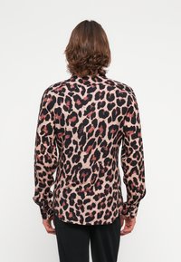 Leopard print shirt with a soft texture, featuring shades of black, tan, and reddish accents. Long sleeves and a buttoned collar.