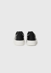 Sneakers in pelle nera con suole in gomma bianca. Caratterizzati da una texture liscia, un design minimalista e un'etichetta sul retro.