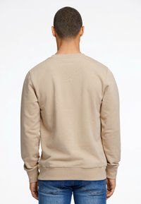 Felpa beige con polsini e orlo a costine, caratterizzata da una texture liscia. La vista posteriore mostra un design semplice senza grafiche o motivi.
