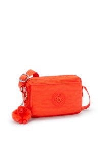 Jasnopomarańczowa torebka crossbody marki Kipling wykonana z teksturowanej tkaniny, z przednią kieszenią, plecionym paskiem oraz futrzanym breloczkiem w kształcie małpki.