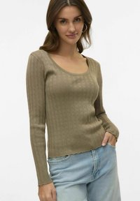 Olivgrön ribbad långärmad topp med rundad nacke och vågig nederkant. Mjuk, texturerad stickning med en figurnära silhuett. Jeans synliga nedanför.