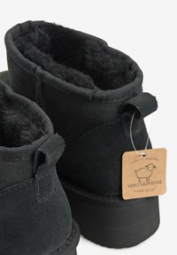 Czarne zamszowe botki za kostkę z miękką podszewką, grubą podeszwą i metką przymocowaną do buta. Charakteryzują się gładką fakturą i subtelnymi detalami szwu.