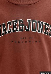 Sweatshirt en coton marron arborant le logo "JACK&JONES" en texte blanc et noir en gras, avec un texte plus petit indiquant "EST. 90 WORLDWIDE" en dessous.