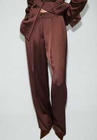 Braune Satin-Anzughose mit weitem Bein. Glatte Textur, taillierte Passform und dezent Falten. Kombiniert mit spitzen Absatzschuhen.