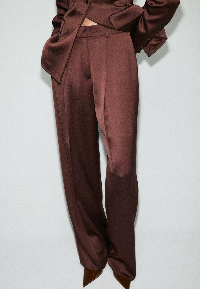 Braune Satin-Anzughose mit weitem Bein. Glatte Textur, taillierte Passform und dezent Falten. Kombiniert mit spitzen Absatzschuhen.