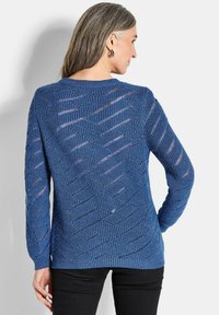 Blauer Strickpullover mit einem strukturierten, durchbrochenen Muster. Lange Ärmel und ein runder Ausschnitt. Kombination mit schwarzen Hosen.