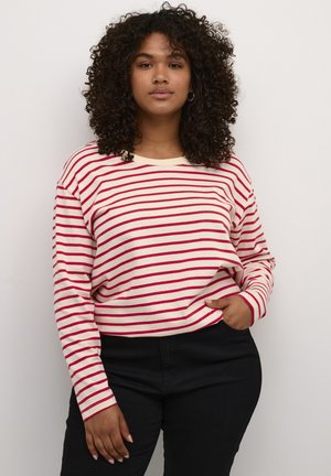 Long-sleeve, cream shirt with red stripes, featuring a relaxed fit and crew neckline. Paired with black pants, showcasing a casual style.