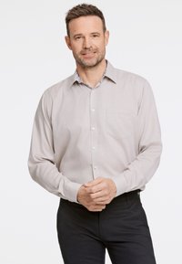 Jasno beżowa koszula z długim rękawem, zapinana na guziki, z delikatną fakturą i kwiatowym wzorem wewnątrz kołnierzyka. Widoczna jedna kieszeń na piersi.