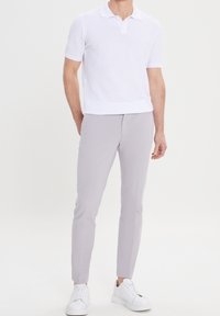 White short-sleeve polo shirt with a textured fabric, paired with light gray slim-fit trousers and white sneakers.