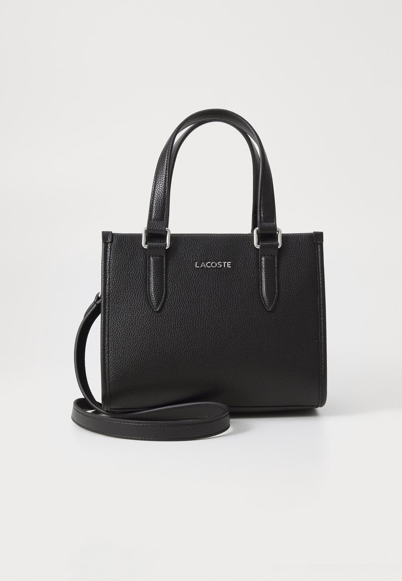 Sac à main Lacoste en cuir noir texturé avec doubles poignées, bandoulière amovible et logo argenté à l'avant.