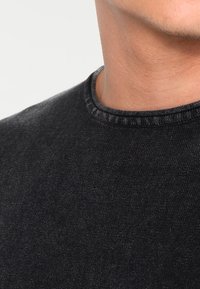 Camiseta negra de algodón con cuello redondeado, presenta una textura sutil. Vista en primer plano que se centra en las costuras del cuello y los detalles del tejido.