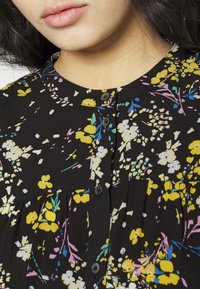 Blusa preta com estampas amarelas, rosas e azuis, decote redondo, botões na parte da frente e franzido no peito.