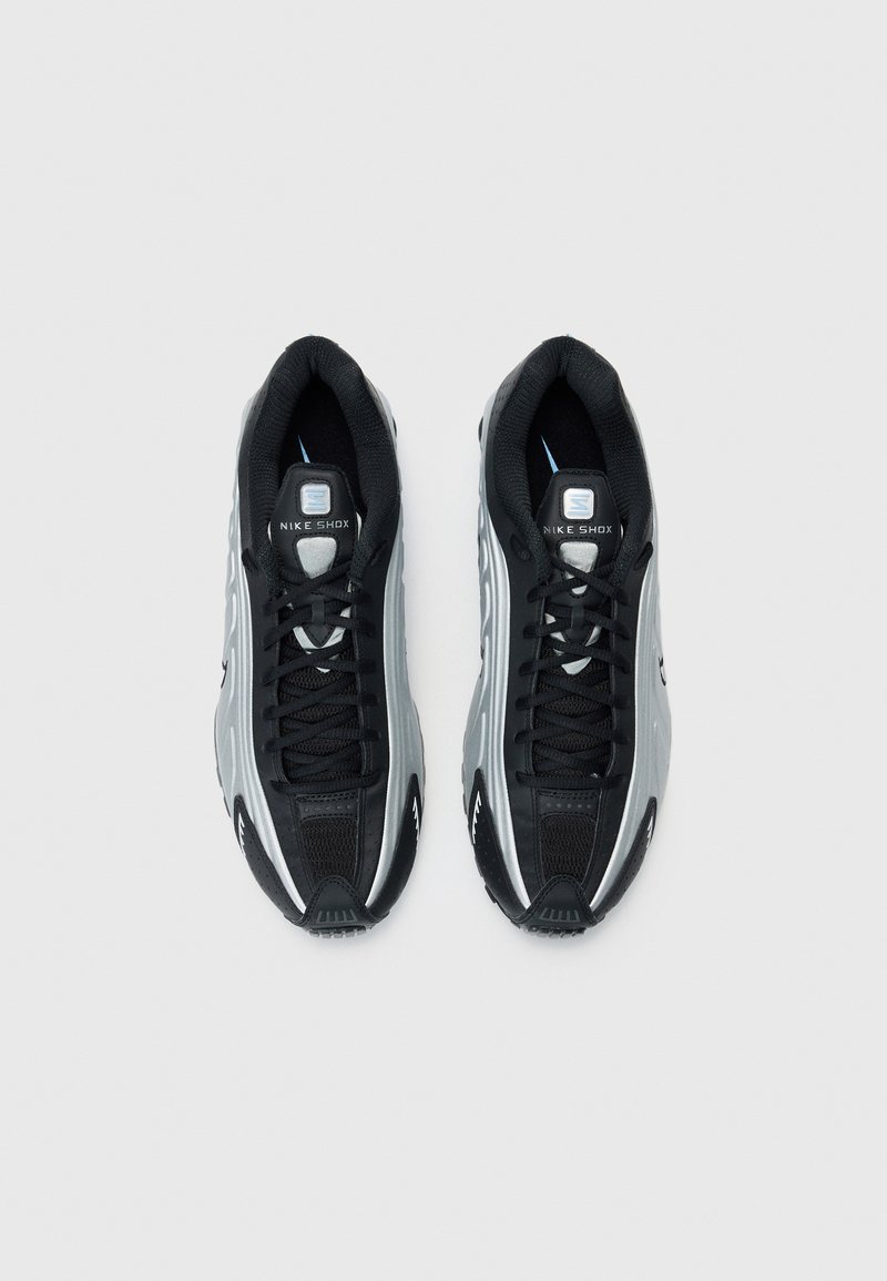 Zapatillas Nike Shox en negro y gris con parte superior de malla, cierre con cordones, cuello acolchado y un diseño de suela distintivo con amortiguación visible.