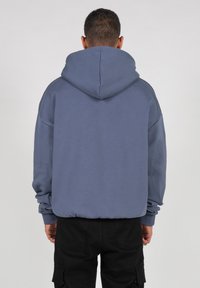 Blue hooded sweatshirt with a relaxed fit, ribbed cuffs, and a smooth texture. Features a large hood, visible stitching, and no graphics.