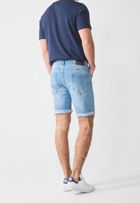 Světle modré denimové šortky s ohrnutými lemy, mají zadní kapsy a hnědou koženou nášivku na pásu; nošeny s námořnickým tričkem.