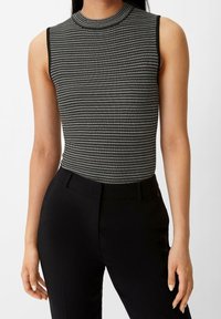 Czarnobiała, bezrękawnikowa, prążkowana bluzka z wysokim kołnierzem, z geometrycznym wzorem i subtelną fakturą. W połączeniu z czarnymi, wysokim stanem spodniami.