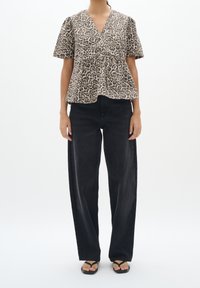Top corto a maniche corte con stampa leopardata in beige e marrone, con scollo a V e davanti plissettato, abbinato a jeans neri a gamba larga a vita alta e infradito.
