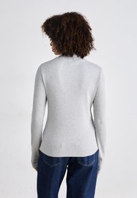Gray long-sleeve sweater with a subtle ribbed texture and a rounded neckline, paired with dark blue wide-leg jeans.