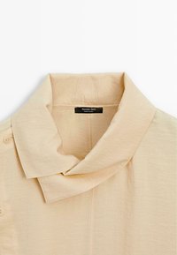 Beige overhemd met kraag en een zachte textuur, voorzien van knopen aan de voorkant en een label met de tekst "Massimo Dutti, Made in China".