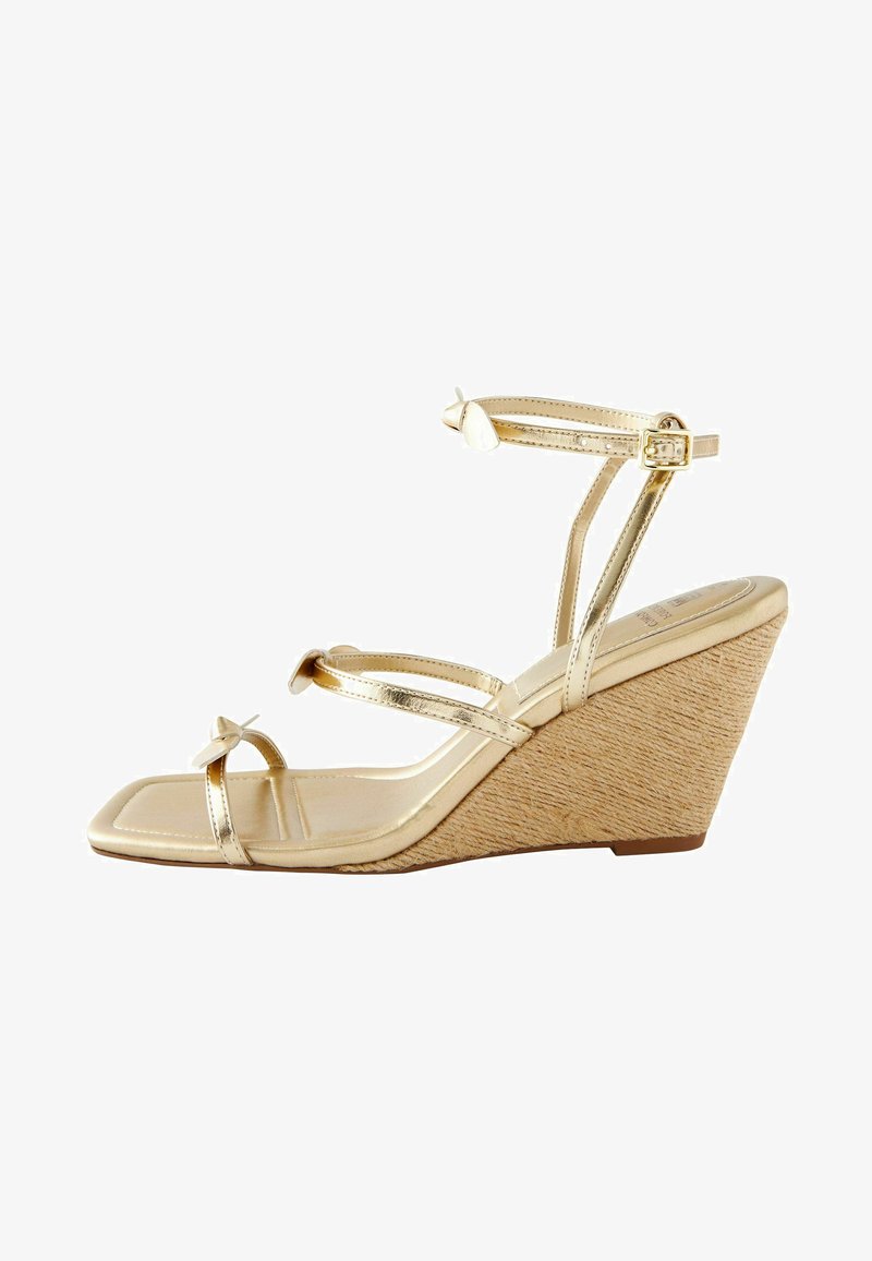 Zlatne wedges sandale s tankim trakama i detaljem mašne. Imaju četvrtasti vrh i teksturiranu, tkanu platformu. Podesiva narukvica oko noge.