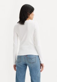 Weißes Langarmshirt mit Rundhalsausschnitt, aus dünnem Stoff gefertigt. Kombiniert mit hellblauen, locker sitzenden Jeans aus Denim, die über ein Design mit Gesäßtasche verfügen.