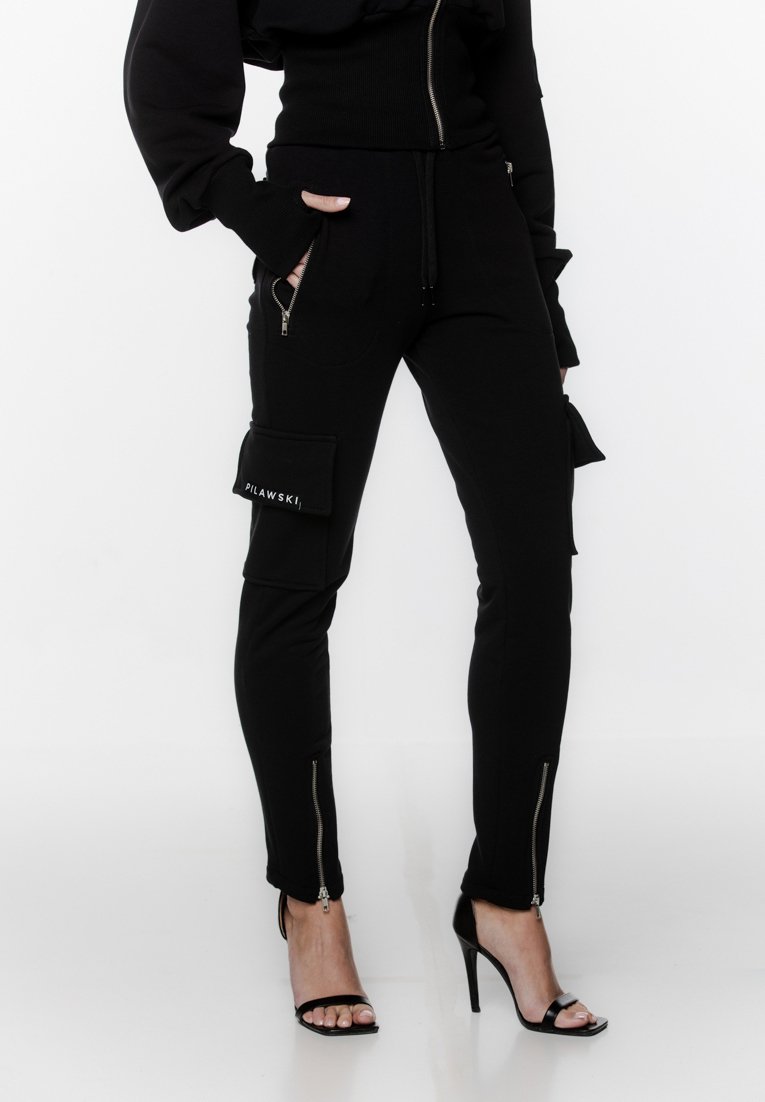 Czarne spodnie cargo z bocznymi kieszeniami i zamkami błyskawicznymi u dołu, wykonane z miękkiego materiału. Posiadają widoczną łatkę z logo na kieszeni.