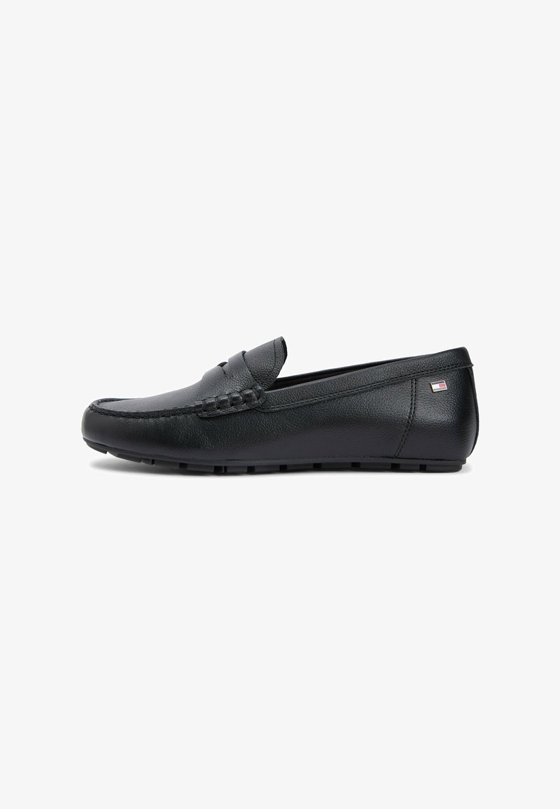 Black leather slip-on loafer with stitched detailing and a small rectangular flag emblem near the heel on a white background.