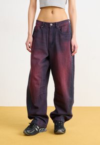 Baggy denim jeans with a gradient from dark purple to burgundy. Features large pockets and side stripes, paired with black sneakers.