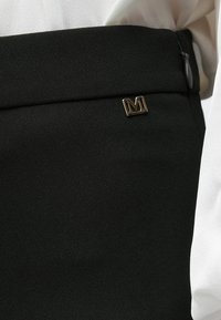 Μαύρη υφασμάτινη φούστα με ομαλή υφή, που διαθέτει χρυσό μεταλλικό λογότυπο "M" και κρυφό φερμουάρ στο πλάι.