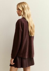 Bordeaux, texturerad stickad tröja med en avslappnad passform, ihop med en plisserad mörk kjol. Långt, rakt blont hår syns.