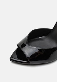 Sandale à talon haut en cuir verni noir, à bout ouvert, avec une large bride sur les orteils et une semelle intérieure rembourrée et lisse.