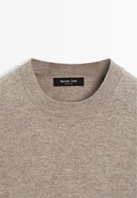 Beżowy sweter z okrągłym dekoltem, wykonany z miękkiej dzianiny. Posiada ribbrowany kołnierz i dół, z czarną metką z napisem "Massimo Dutti."