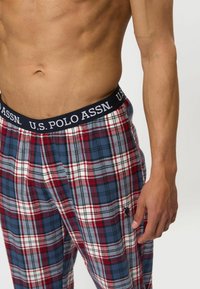 Geruite loungebroek in rood, blauw en wit. Heeft een marineblauwe tailleband met de tekst "U.S. POLO ASSN." en een klein geborduurd logo op het been.