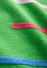 Green fabric with a soft texture featuring horizontal stripes in pink and blue. The design includes a distinct red accent.