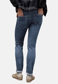 Mörkblå jeans i denim med smal passform, som har två bakfickor och uppvikta fållar, kombinerade med beige sneakers och vita strumpor.
