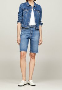 Jeansjacka med klassisk passform, ljusblå färg, framfickor, knappar, kombinerad med matchande blå denimshorts och vita slip-on skor.