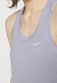 Top atletico senza maniche di colore viola chiaro con scollatura rotonda e un piccolo logo Nike silver sulla parte sinistra del petto. Tessuto dalla texture liscia.