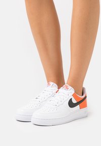 Vita lädersneakers med svart swoosh, orange detalj, perforerat tåparti och vit gummisula. Har vadderad krage och snören.