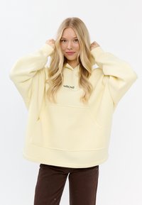Geel oversized hoodie gemaakt van zachte stof, met een voork pocket en een subtiele groene logo. Lange mouwen met een relaxte pasvorm.
